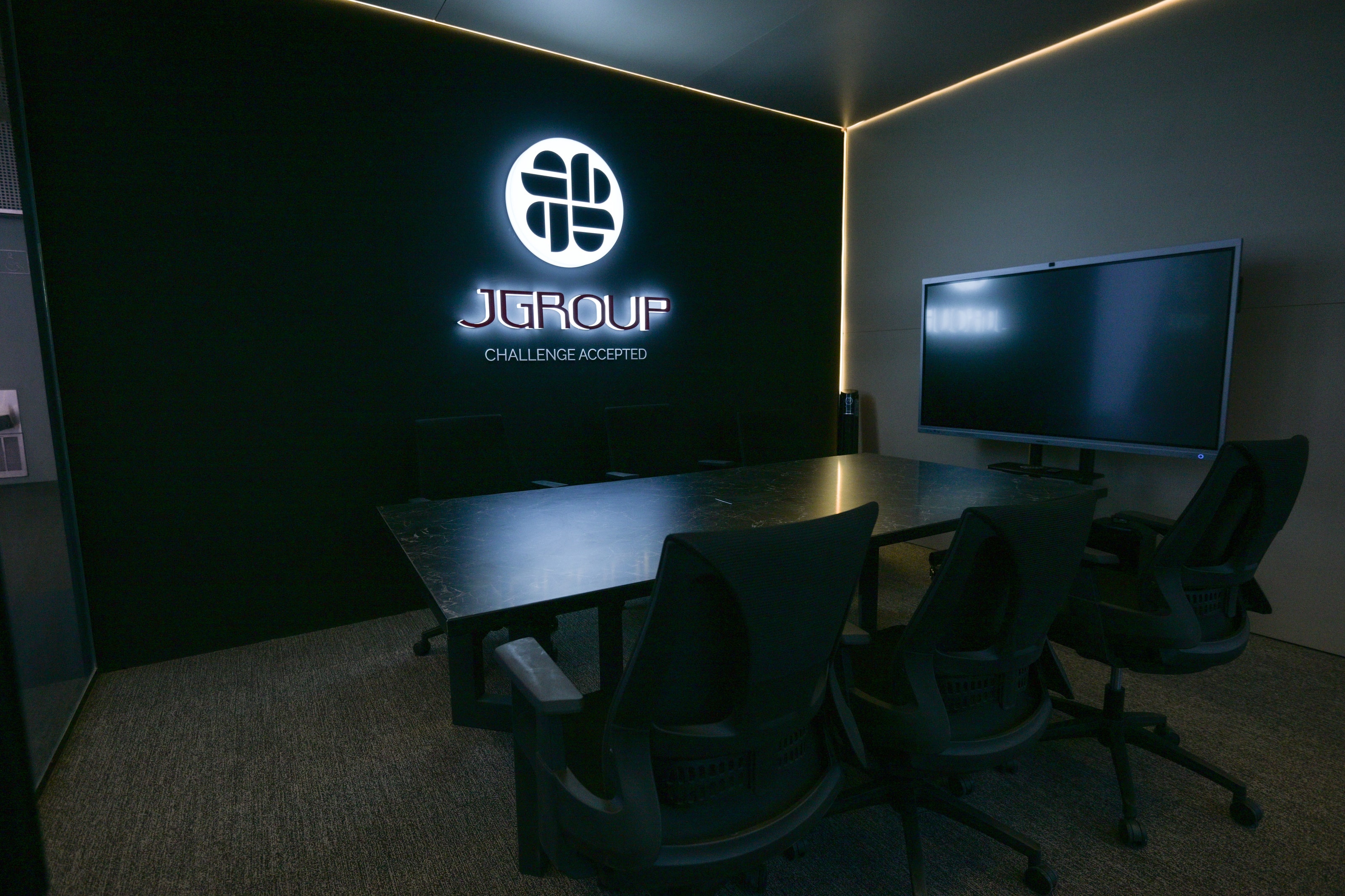 Meeting room with a wall screen and the J Group logo